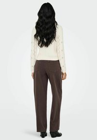 Pull en tricot blanc avec des motifs complexes et des accents floraux ; pantalon large marron ; mannequin de dos, portant des talons noirs.