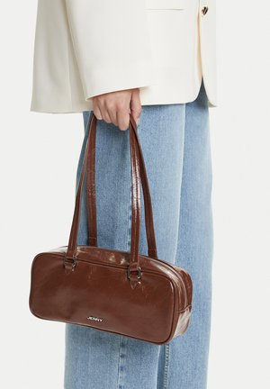 Person wearing light blue jeans and white blazer holding a brown rectangular leather handbag with double straps and zipper closure.