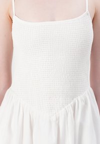 White dress with a textured smocked bodice and a flowing skirt. Features thin spaghetti straps and a soft, lightweight fabric.