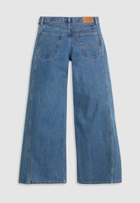 Jeans de denim azul de perna larga com uma cintura de altura média, dois bolsos traseiros e um patch de marca em pele na parte de trás da cintura, apresentando uma textura de lavagem desbotada.