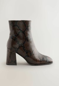 Pruun ja must ärakaupa mustriga pahkluudega saapad, millel on plokknina, heledal taustal, külgvaade.