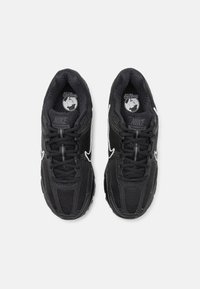 Svarta Nike-sneakers har en texturerad ovandel med mesh och syntetiska material, rund tå och vita detaljer längs sidorna och snörningen.