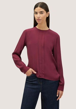 Bordeaux lange mouwen blouse met een ronde halslijn, verticale plooien en knoopmanchetten, gecombineerd met donkere denim jeans. Zachte textuur.