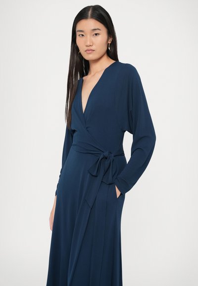 Tumši zila apvijas kleita no gludas auduma ar garām piedurknēm, dziļu V-veida izgriezumu, sasienamu jostu un sānu kabatām.