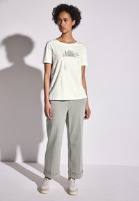 Camiseta color beige claro con un estampado gráfico, combinada con pantalones de chándal gris claro de corte holgado y zapatillas blancas. La textura parece suave.