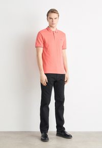 Korálová polo košile s vroubkovaným límcem a dvoubarevným zapínáním, v kombinaci s černými slim-fit kalhotami a lesklými černými botami.