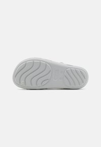 Bílá gumová podešev s texturovanými drážkami, s hladkým povrchem a kulatým detailem značky. Navržena pro trvanlivost a trakci.