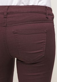 Vaqueros de mezclilla color burdeos vistos desde atrás, con un pequeño bolsillo trasero moldeado y una textura suave, y con costuras planas a lo largo de la cinturilla.