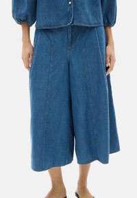 Pantalones culotte de mezclilla azul claro con silueta en A, de largo hasta la mitad de la pantorrilla, que presentan costuras frontales y una textura suave, terminados con un dobladillo sin rematar.