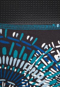 Matériau noir texturé avec des points en relief en haut, présentant des motifs géométriques colorés en teal, bleu et blanc sur un fond sombre.