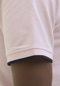 Lys pink polo-shirt stof tæt på, med en tekstureret vævning og mørk navy trim ved ærmeafslutningen.