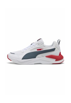 Vit Puma-sneaker med mörkgrå rand, röda accenter på häl och sula, mesh-ovandel och snörning, sedd från sidan.