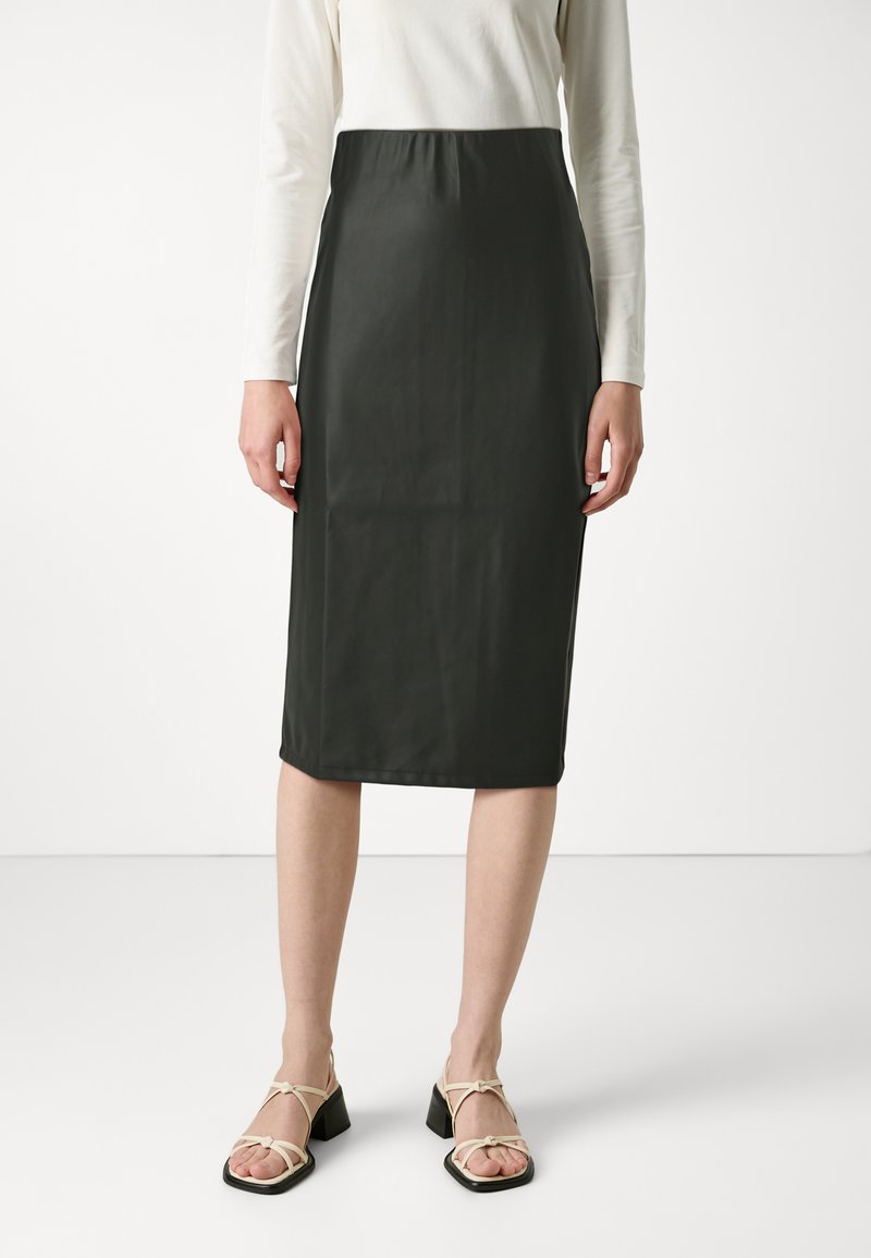 Falda verde oscuro, a la altura de las rodillas, con un acabado suave y mate. Presenta una cintura elástica y se lleva con sandalias de tiras de color claro.