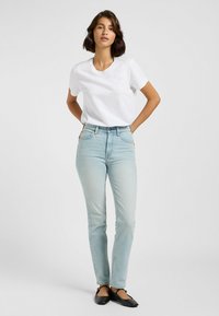 T-shirt bianca in cotone con scollatura a V, abbinata a jeans in denim azzurro chiaro. I jeans hanno una gamba dritta con una finitura sbiadita e un classico design a cinque tasche.