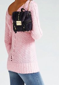 Strikket lyserød sweater med struktureret mønster og sideslidsdetaljer, parret med en sort stofrygsæk med guld accenter og nitter.