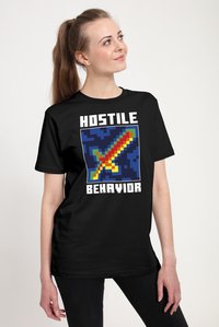 Sort bomulds-T-shirt med et pixeleret sværddesign i rød, gul og blå, med teksten "HOSTILE BEHAVIOR" i fede, hvide bogstaver.