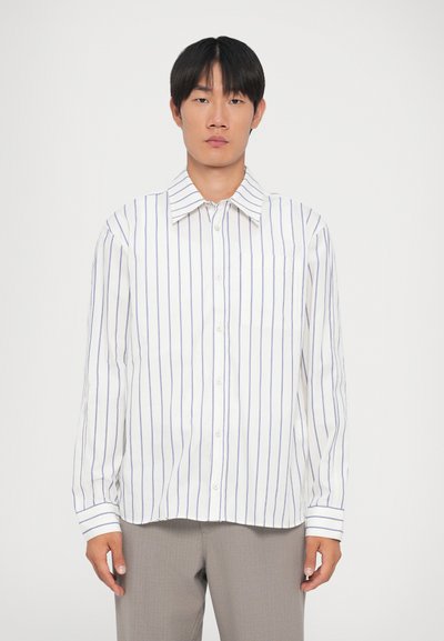 Camisa blanca de manga larga con rayas verticales azules, cierre de botones al frente y cuello estándar. Presenta un bolsillo en el pecho y mangas con puños.