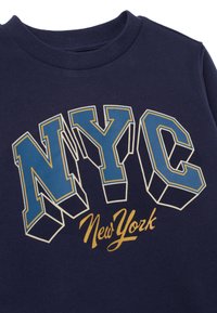 Marineblauwe sweatshirt met gedurfde, 3D-stijl "NYC" in blauw en goud, met schone lijnen en een geribbelde ronde hals.