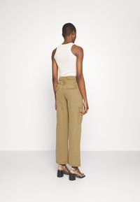 Pantalon cargo beige à coupe décontractée, avec poches latérales et taille haute. Associé à des sandales à talons noires avec brides.