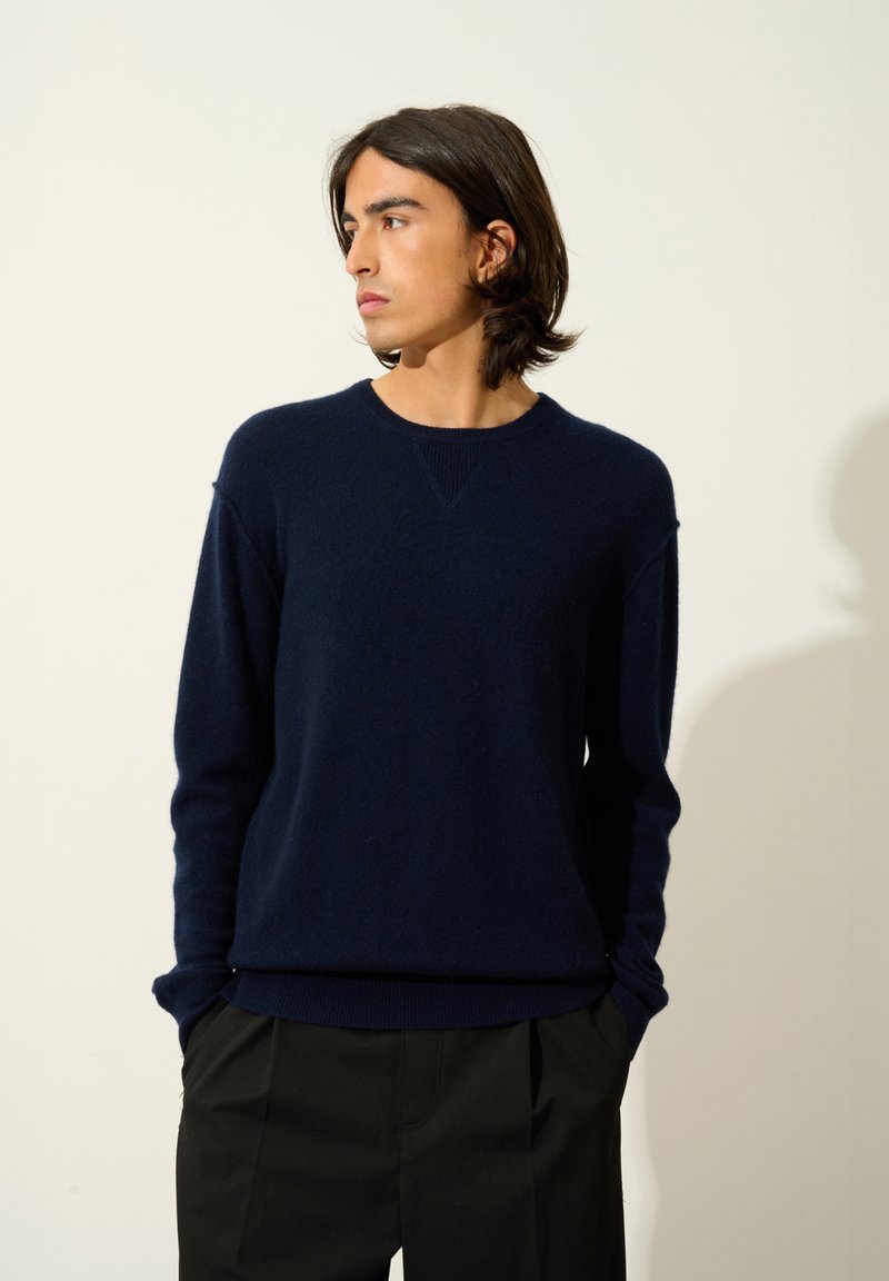 Mörkblå stickad tröja med rund halsringning och ribbat avslut, med en avslappnad passform och långa ärmar. Bärs med svarta avsmalnande byxor.