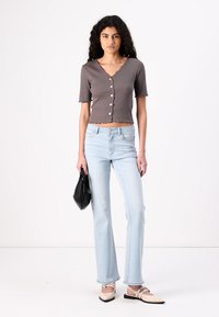 Light gray short-sleeve top with buttons, paired with high-waisted light blue flared jeans and beige slip-on shoes; black handbag in hand.
