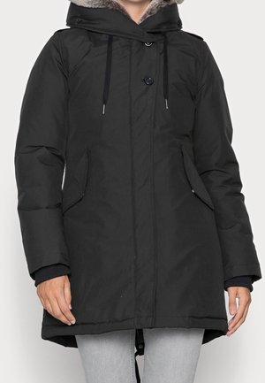 Black hooded winter coat with fur trim, front buttons, drawstrings, and side flap pockets worn over light gray jeans.