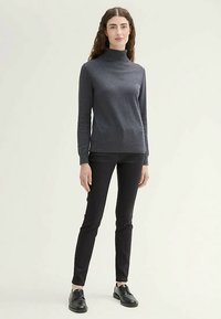 Dunkelgrauer Rollkragenpullover, figurbetontes Design, aus einem weichen Material gefertigt. Kombiniert mit schwarzen Slim-Fit-Hosen und schwarzen Schnürschuhen.