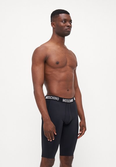 Boxer-briefs noirs en tissu lisse, dotés d'une ceinture élastique de marque avec "MOSCHINO" en blanc. Design ajusté, longueur mi-cuisse.