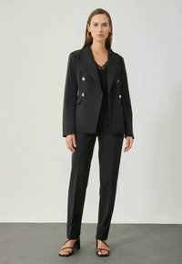 Black tailored blazer with gold buttons, paired with fitted black trousers. Smooth fabric, double-breasted design, and minimalist accents.