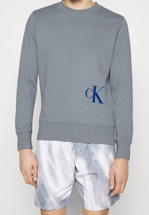 Grauer Sweatshirt mit Rundhals, langen Ärmeln, gerippten Bündchen und Saum. Mit einem blauen 'cK'-Logo auf der unteren Vorderseite links.