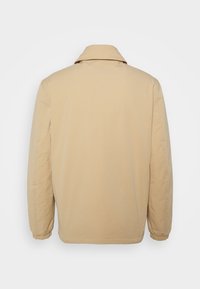 Beige letvægtsjakke med klassisk krave, elastiske manchetter og en glat tekstur, vist bagfra. Enkel design uden pynt.