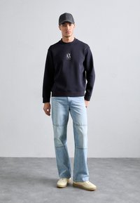 Felpa navy con logo, abbinata a jeans azzurri chiari con cuciture a pannello. Sneakers chiare completano l'outfit.