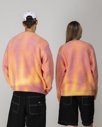 Flauschige, oversized Pullover in einem Farbverlauf von Pink, Orange und Gelb; gerippte Bündchen und Säume; kombiniert mit schwarzen Shorts mit hinteren Taschen.