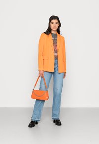 Oransje blazer med to frontlommer over en grafisk t-skjorte, parret med lyseblå flagrende jeans og en oransje håndveske med sølvhardware.