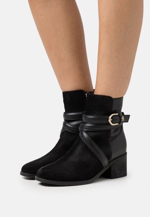 Schwarze Knöchelstiefel aus Leder und Wildleder, mit einem umlaufenden Riemen und einer goldenen Schnalle, quadratischer Zehenform und blockiertem Absatz.