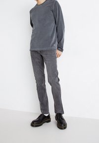 Grå långärmad T-shirt i kombination med mörkgrå slim-fit jeans och svarta snörskor med gula sömmar. Slät tygtextur.