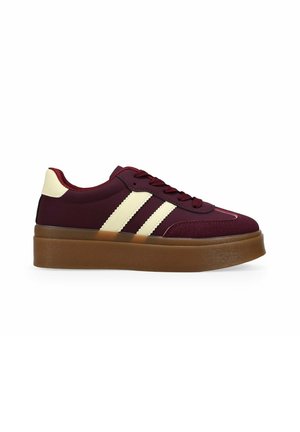 Bordeauxfarbener Sneaker mit cremefarbenen Streifen und Fersenlasche, dicker brauner Plateausohle, Schnürdesign, auf weißem Hintergrund.
