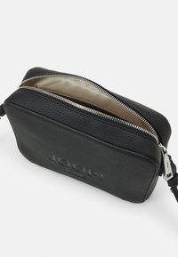Čierna kožená crossbody taška s textúrovaným povrchom, strieborným zipsom a béžovým podšívkou. Na prednej strane sa nachádza embosované logo.