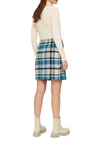 Un pull à col roulé crème associé à une mini-jupe à carreaux bleus, noirs et lavande et des bottines beige clair avec des semelles épaisses.