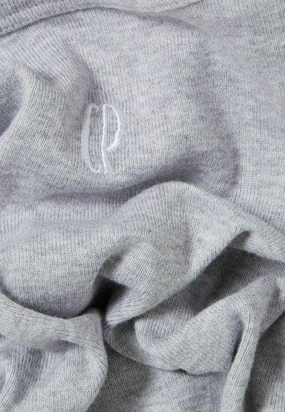 Tessuto a maglia grigia con una consistenza morbida, caratterizzato da un piccolo logo ricamato. Il tessuto presenta un sottile motivo mélange e un aspetto sfilacciato e spiegazzato.