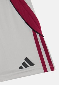 Tela gris con ribete en burdeos y negro, que presenta tres franjas burdeos y un logo negro de Adidas en la esquina inferior.