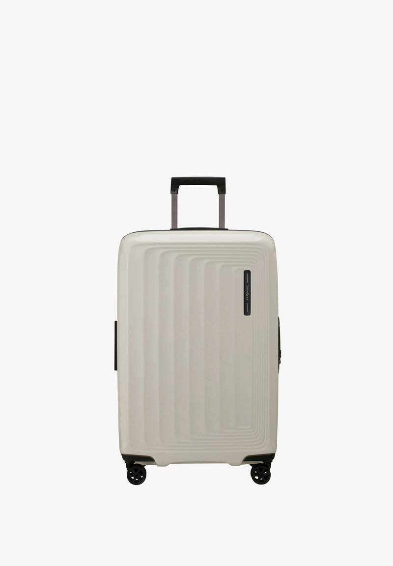 Hartschalentrolley in Elfenbein, mit gerippter Oberfläche, schwarzem Griff und vier drehbaren Rollen für einfache Mobilität.