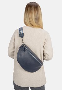 Marineblaue Leder-Crossbody-Tasche mit strukturiertem Oberflächenmaterial, ausgestattet mit einem gemusterten Schulterriemen und einem Reißverschluss. Die abgerundete Form verbessert die Funktionalität.