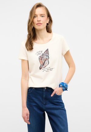 Cremfarbener T-Shirt mit kurzen Ärmeln, versehen mit einem Muschel-Graphic und Text. Kombiniert mit dunkelblauen Jeans und einem blauen, gemusterten Bandana am Handgelenk.