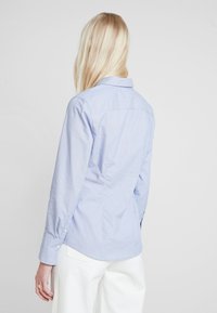 Jasnoniebieska koszula na guziki z długimi rękawami, z charakterystycznym kołnierzykiem, karczkiem z tyłu oraz delikatnymi pionowymi paskami.