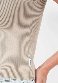 Top a canottiera a coste beige con un design aderente e una texture orizzontale. Presenta un piccolo etichetta laterale con il marchio "SIXTH June".