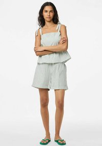 Ensemble en deux pièces rayé avec un décolleté carré, des bretelles réglables, une coupe ample et un short assorti. Des tongs vertes complètent le look.