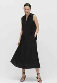 Ensemble composé d'un haut sans manches noir et d'une jupe longue, avec un motif texturé, un col et un ourlet assorti, accompagné de sandales noires fines.