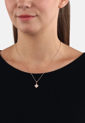 Collana in oro rosa con un piccolo pendente a forma di diamante caratterizzato da un motivo a griglia, indossata su una catena sottile, poggiata su una maglietta nera.