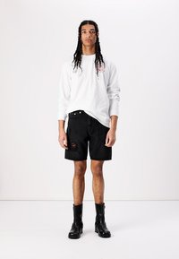 Langærmet hvid skjorte med print på siden, parret med sorte denim shorts med slidser. Sorte ankelstøvler fuldender looket.